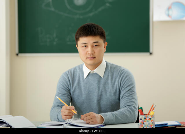 Handsome Asian teacher sitting in classroom Stock Photo - Alamy