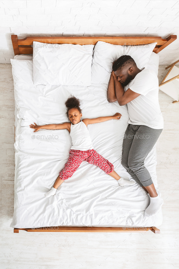 Little african girl lying like star on big parent bed, her daddy ...