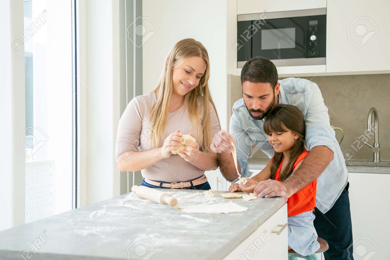 Happy Mom And Dad Teaching Daughter To Knead Dough At Kitchen ...