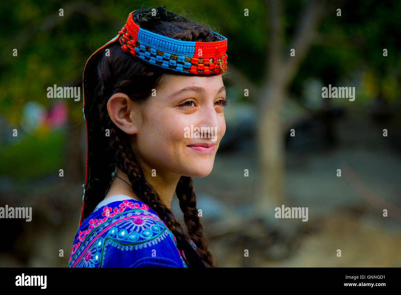 A beautiful Kalasha girl smiles as she passes a forest in Kalash ...