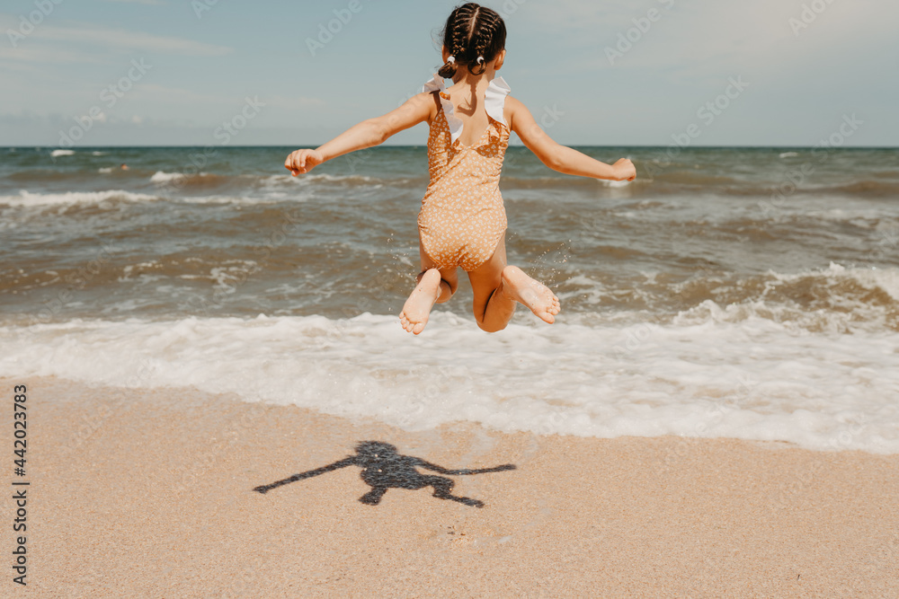 Six year girl in yellow swimsuit jumping on the beach, people from ...