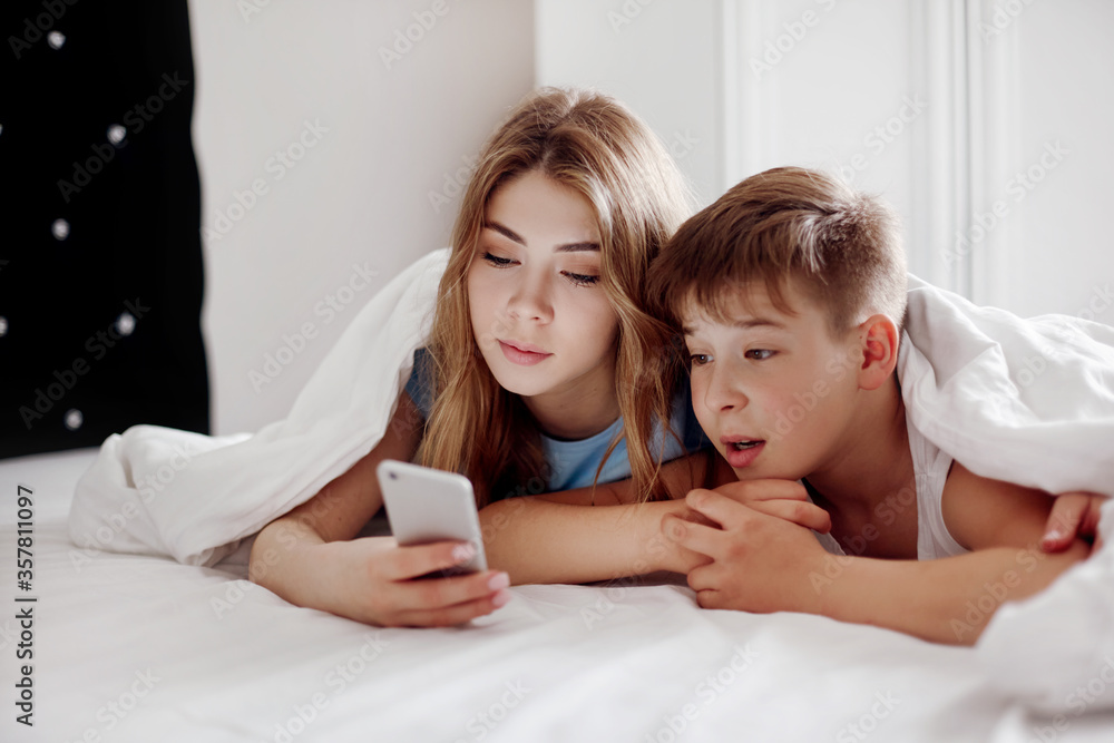 A young girl shows her younger brother a video on her phone while ...